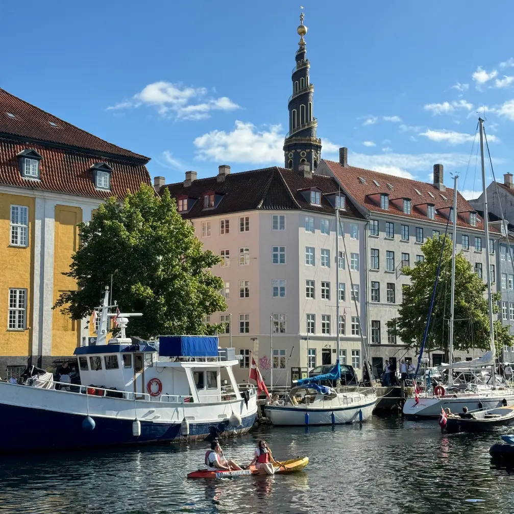 Christianshavn canal with boats, a couple on a kayak, and the spire of the Church of Our Saviour
